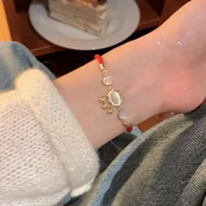 Close-up detail shot of a red cord bracelet with gold charms and white beads on wrist
