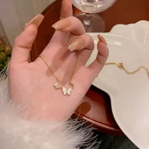 Délicat collier avec pendentif double papillon en acier titane tenu par une main gros plan