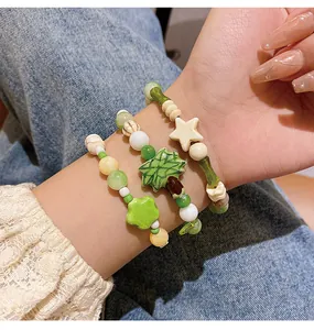 Vista detallada de pulseras de cuentas de cerámica verde macaron con colgantes de hojas.