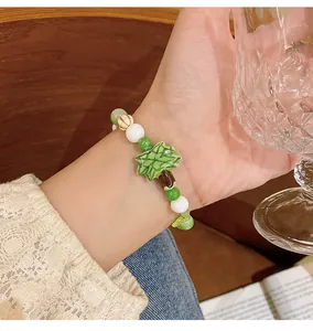 Detalle de una pulsera de cuentas de cerámica con dije de hoja verde en la muñeca