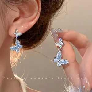 Close-up of blue gradient crystal butterfly drop earrings on ear and hand.