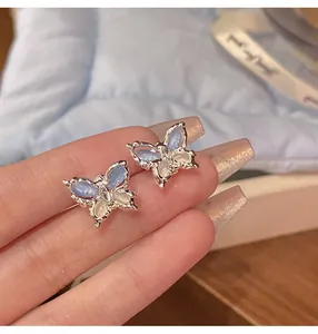 Close-up view of delicate butterfly stud earrings with blue and white inlaid wings.
