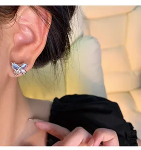 Detail view of elegant silver butterfly stud earrings with blue opal-like wings on ear