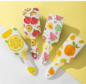 Detailed view of four colorful fruit-patterned paddle hairbrushes on a yellow background