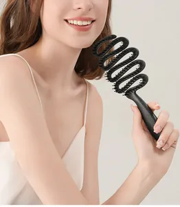 Woman holding a black speckled ribbon-shaped boar bristle hairbrush for detangling hair.