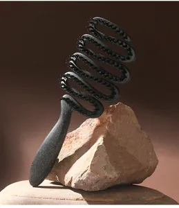 Detailed shot of a black speckled spiral hairbrush resting on a natural rock prop.