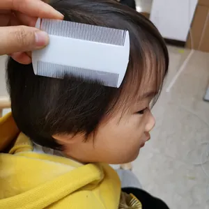 Detailed view of a white plastic double-sided fine-tooth nit comb being used