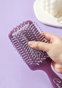 Close-up of purple square totem print air cushion hairbrush being pressed by hand