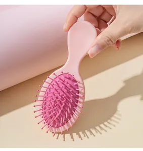A hand holding a cute mini pink air cushion paddle hairbrush for girls and kids