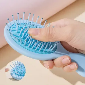 Portable light blue air cushion hairbrush being pressed to demonstrate its soft and resilient teeth