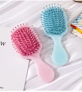 Close-up of pearlescent pink and blue mini air cushion hairbrushes on white silk fabric.