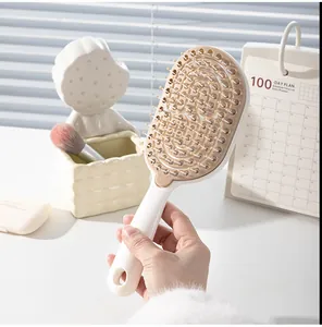 Primer plano de una mano sosteniendo un cepillo de pelo masajeador beige.