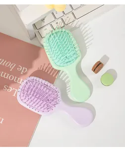 Two mini pastel air cushion hairbrushes on a desk with cute accessories and keyboard