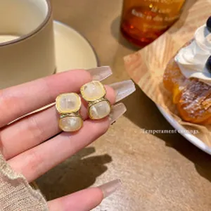 Elegante gouden geometrische oorknopjes met marmerpatroon steen in de hand gehouden