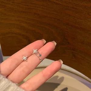 Detail shot of dainty asymmetric silver star earrings with micro-set crystals on a hand