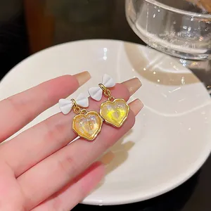 Macro view of heart-shaped earrings with white bow and gold-framed yellow center.