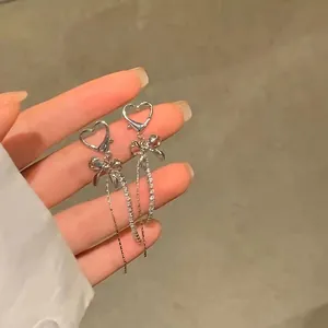Detailed close-up of asymmetric silver long tassel earrings with heart and bow design