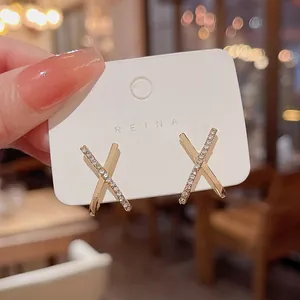 Detail view of X-shaped gold earrings with micro-pave stones on a display card