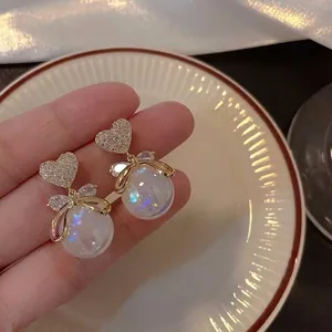 Close-up of elegant gold heart-shaped earrings with crystal bow and iridescent pearl drop