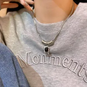 Close-up of titanium steel necklace with black gemstone pendant on gray sweatshirt