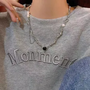Close-up of titanium steel necklace with pearls and a black heart pendant on a model