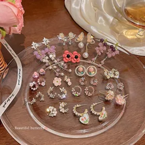 Detailed view of various floral and butterfly earrings arranged on a glass plate.