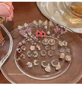 Detailed macro view of various floral and butterfly earrings on an elegant glass plate
