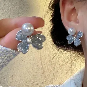 Close-up of elegant glittery blue butterfly earrings with a white pearl on an ear