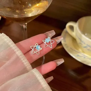 Elegante silberne Sternohrstecker mit hellblauem Zentrum auf Fingern in gemütlichem Ambiente