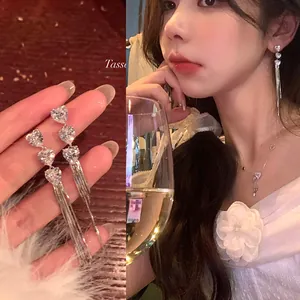 Detail view of heart zircon tassel earrings on hand and worn by model