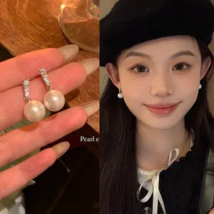 Close-up detail of white pearl earrings with sparkling zircon worn by an Asian model