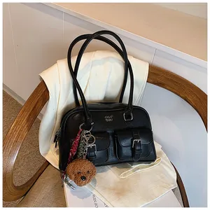 Primer plano de un bolso de hombro vintage negro con múltiples bolsillos y amuleto de oso