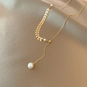 Close-up of elegant gold wheat leaf necklace with dangling pearl detail