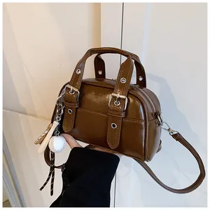 Close-up of a retro brown leather handbag with a baseball charm and silver buckles