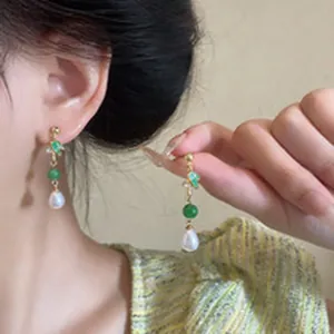 Detailed shot of elegant earrings with green beads and teardrop pearls worn by model