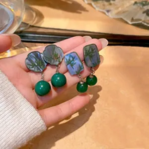 Hand holding vintage green stud earrings with bamboo pattern and round ball pendants