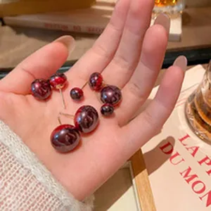 Close-up of dark red pearl-style earrings held in a hand for size comparison