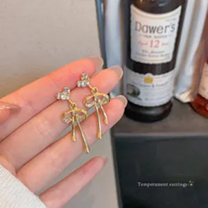 Elegant golden bow earrings with sparkling rhinestones shown held against a blurred background