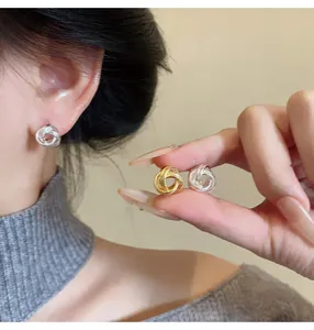 Close-up detail of stylish twisted metal knot stud earrings in gold and silver finishes.