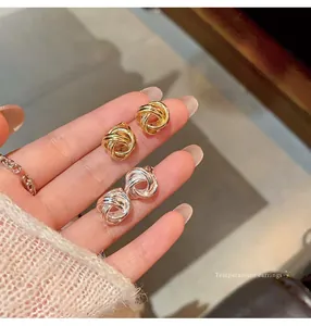 Close-up detail of gold and silver twisted knot metal stud earrings held on fingers