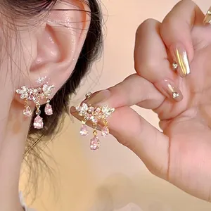 Close-up of pink flower earrings with teardrop tassels on ear and held by hand