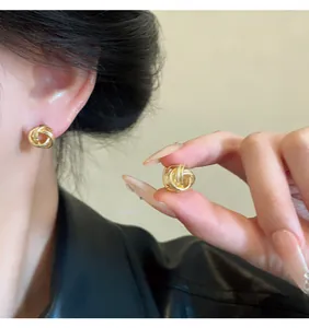Detailed view showing the elegant gold twisted knot stud earrings worn and held by a model.