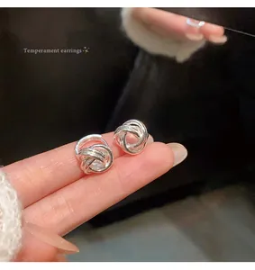 Detail shot of elegant silver-tone twisted metal knot stud earrings on fingertips