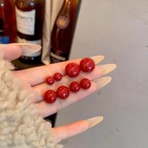 Detailed close-up of vibrant red pearl stud earrings in various sizes held in hand
