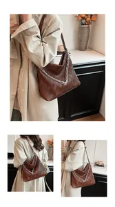 Detailed view of large brown textured tote bag with silver chain strap worn on shoulder