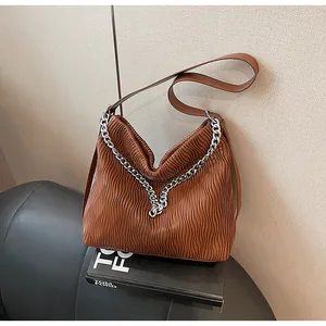 Detailed view of brown pleated hobo bag with silver chain on black book backdrop.