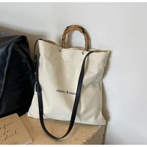 Detail of cream canvas tote bag featuring natural bamboo handle and black strap