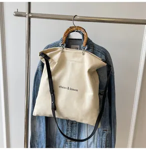 Detailed view of a stylish canvas tote bag featuring a natural bamboo handle and logo.