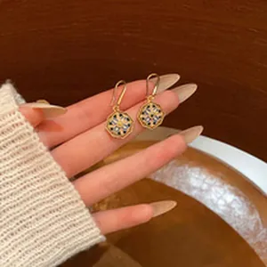 Close-up of gold-toned octagonal dangle earrings with blue floral pattern on fingers