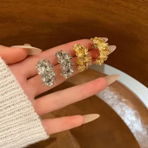 Detailed view of silver and gold sparkling floral cluster earrings held in hand for scale.